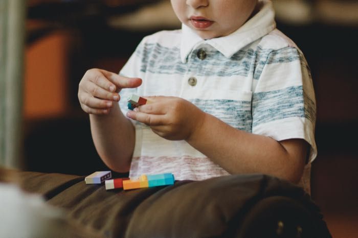 A young boy is sitting on a couch playing with lego blocks.