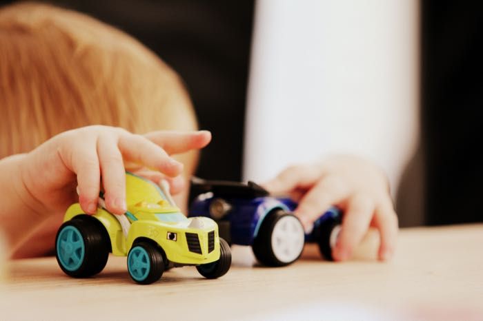 A child is playing with three toy cars on a table.