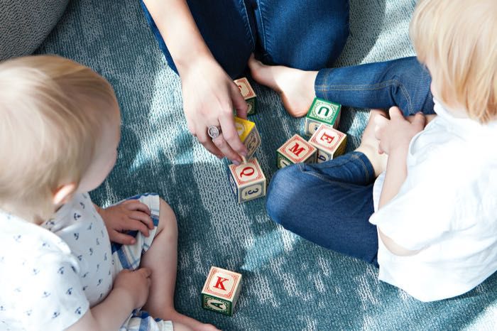 A woman and two babies are playing with wooden blocks on the floor.