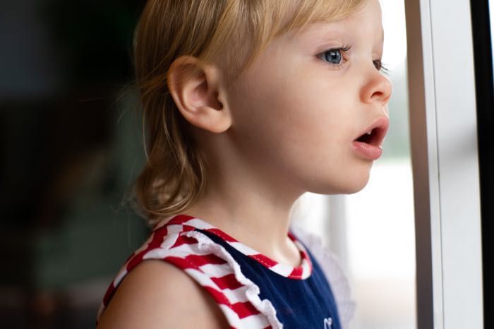 A little girl is looking out of a window with her mouth open.