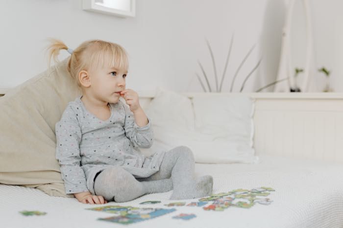 A little girl is sitting on a bed playing with puzzles.