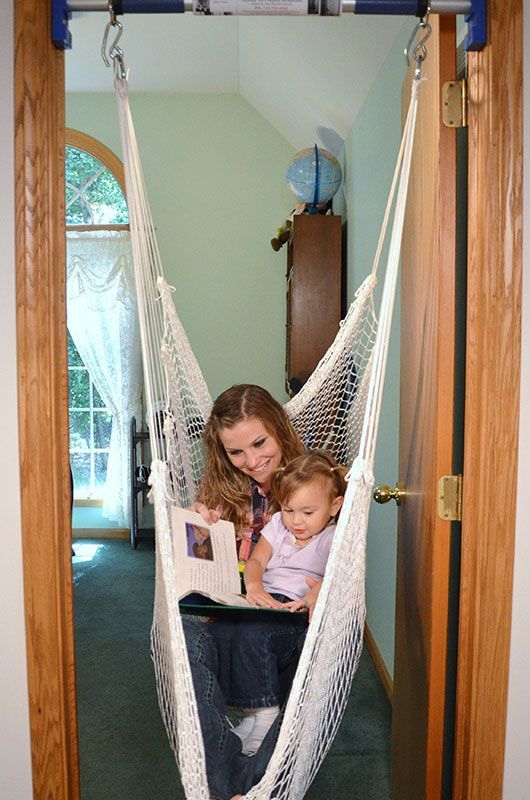 A woman is reading a book to a baby in a hammock.