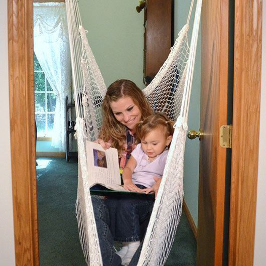 A woman and child are sitting in a hammock reading a book