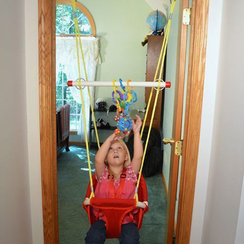 A little girl is sitting in a red swing holding a toy