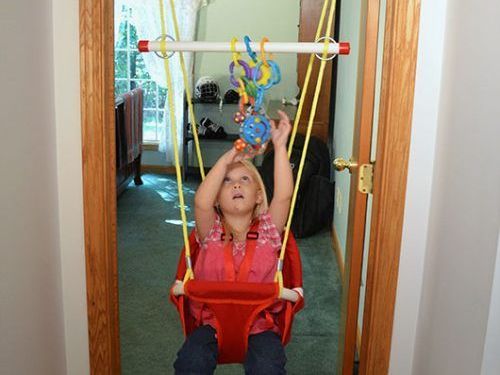 A little girl is sitting in a red swing holding a toy