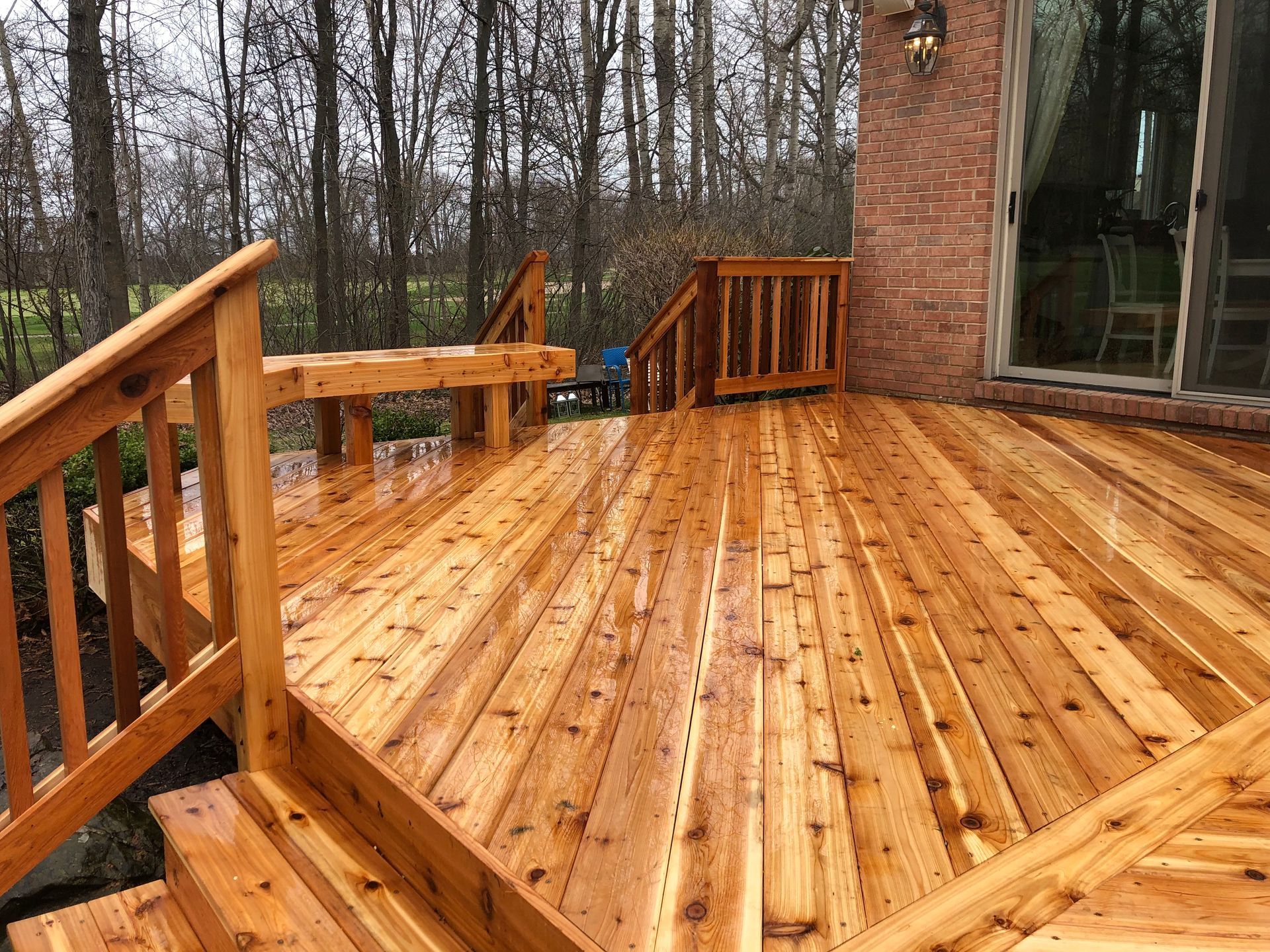 A wooden deck with stairs leading up to it and a brick building in the background.