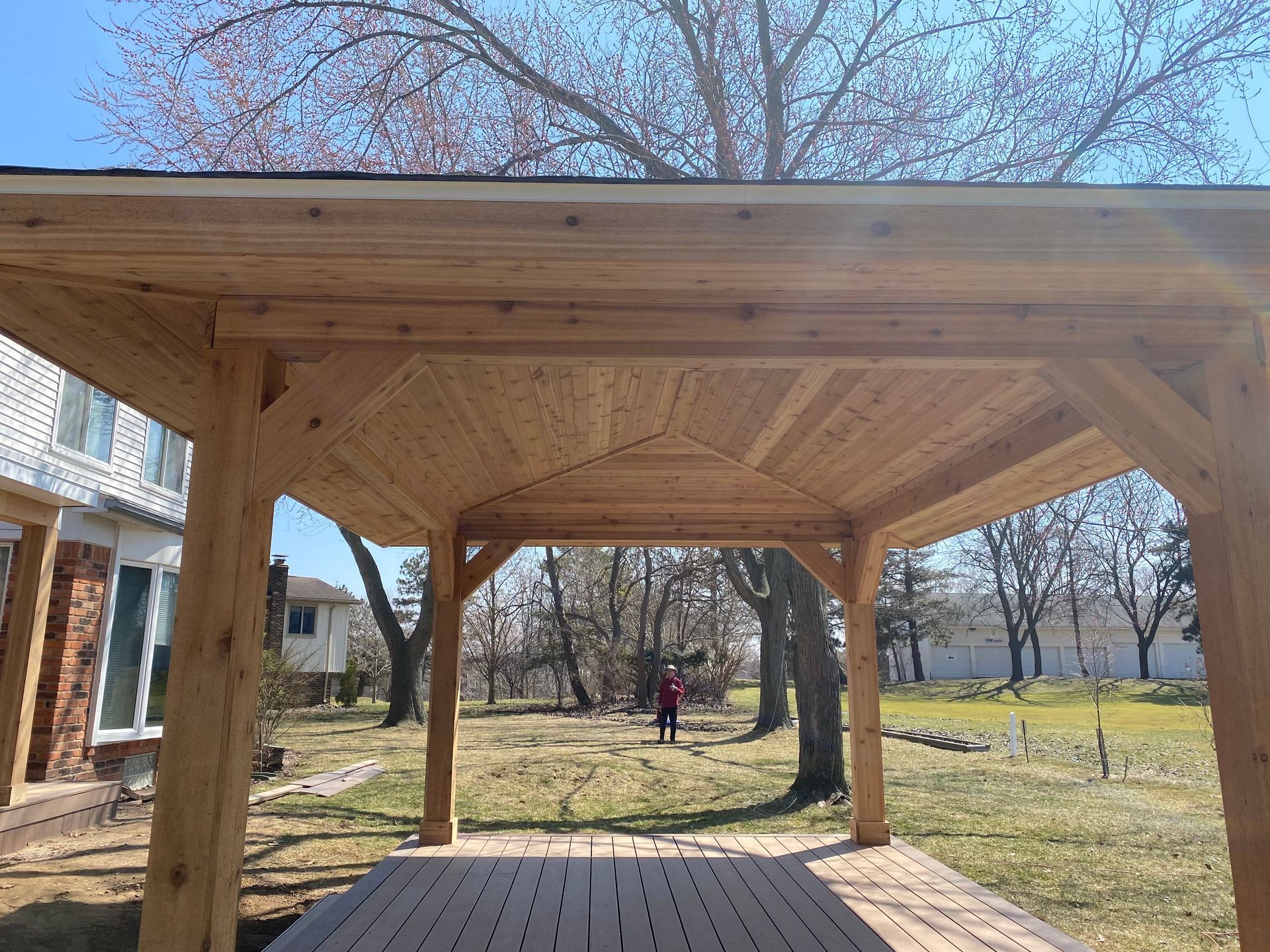 A man is standing under a wooden gazebo in a backyard.