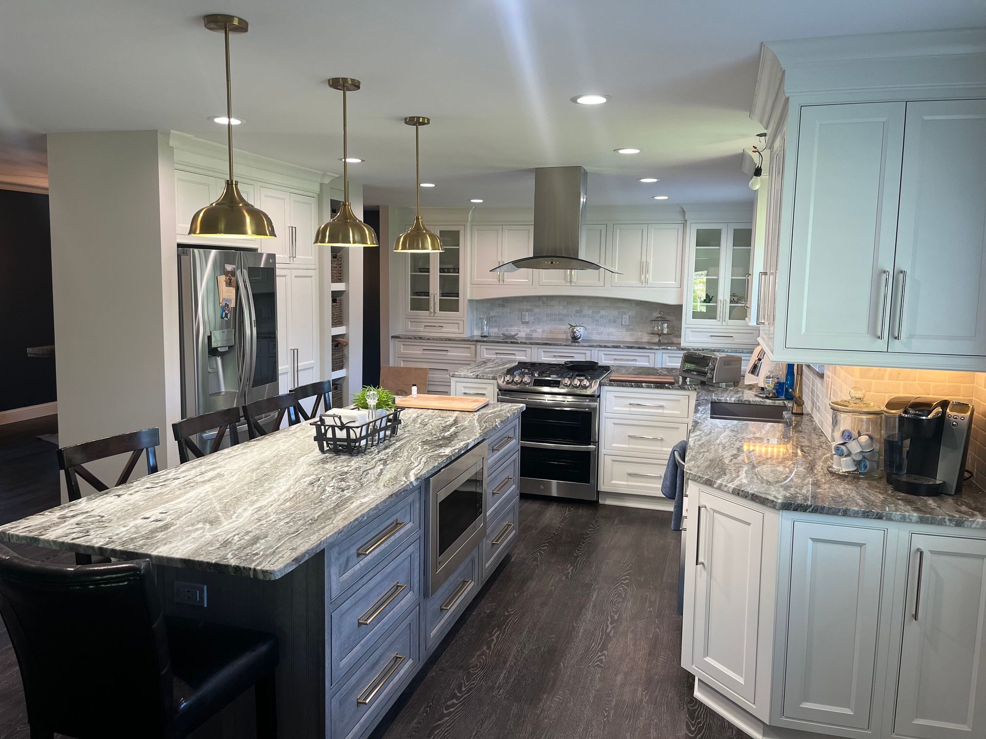 A kitchen with white cabinets , granite counter tops , stainless steel appliances and a large island.