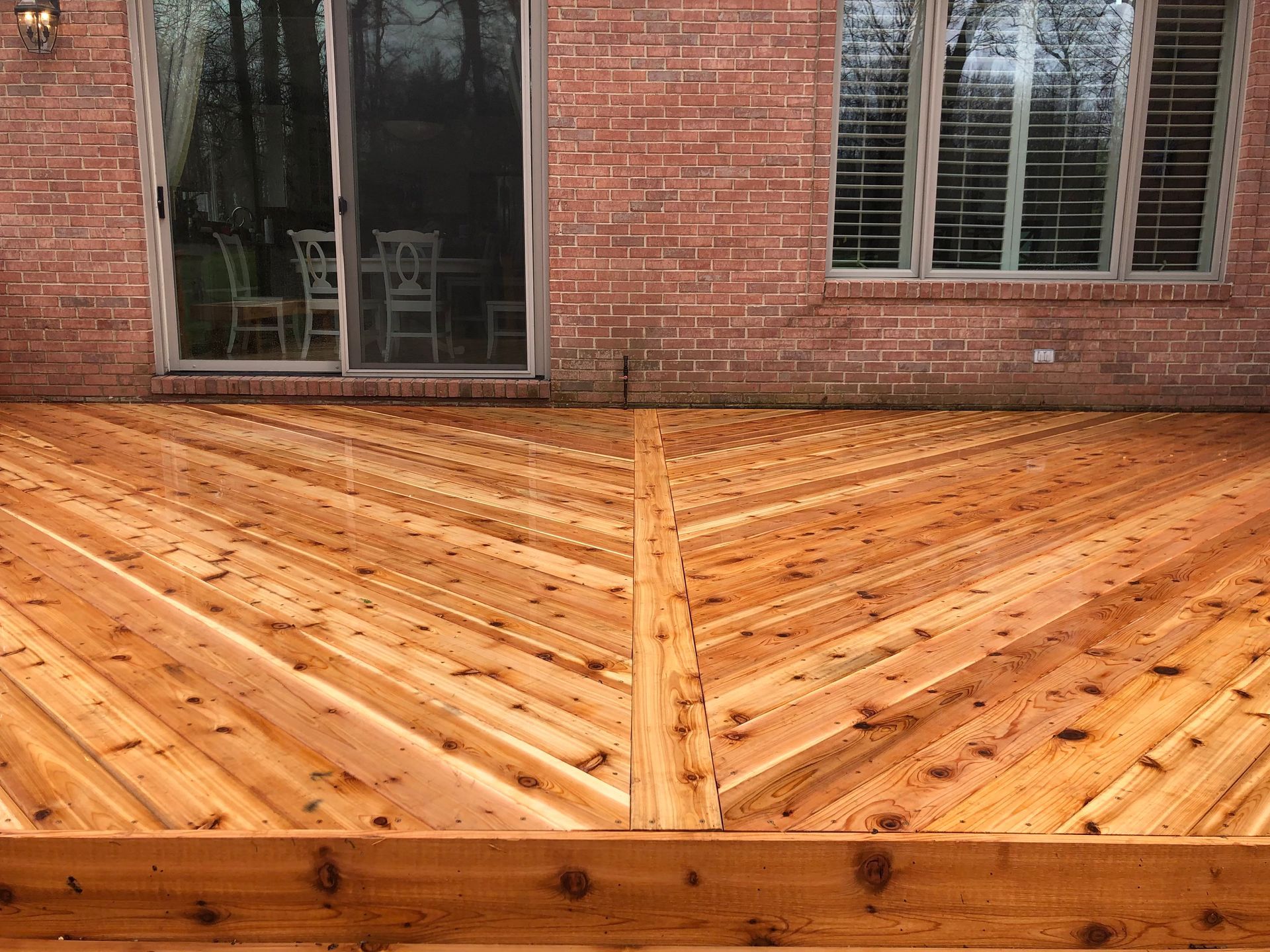 A wooden deck in front of a brick house with a sliding glass door.