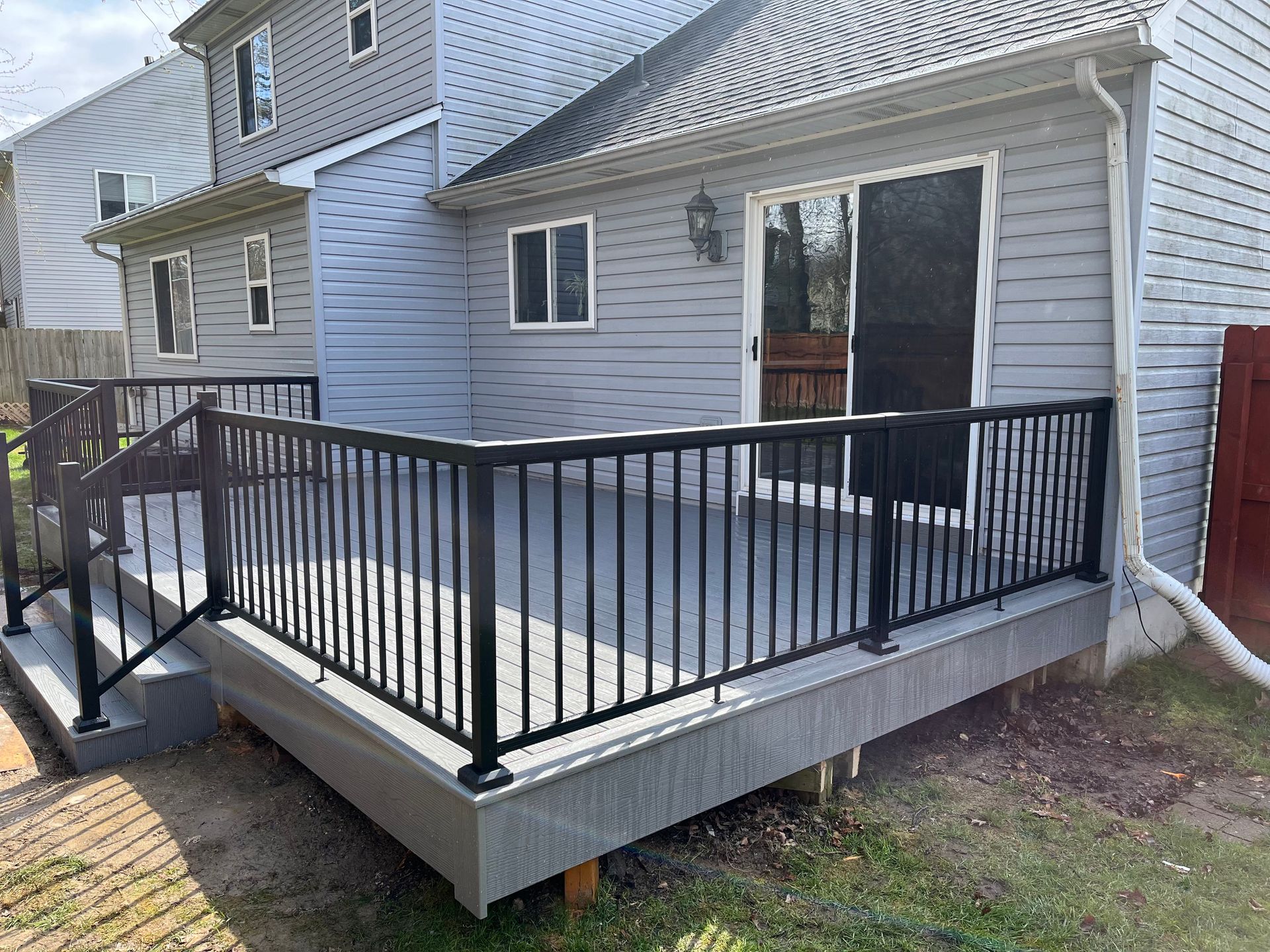 A deck with a black railing is in the backyard of a house.