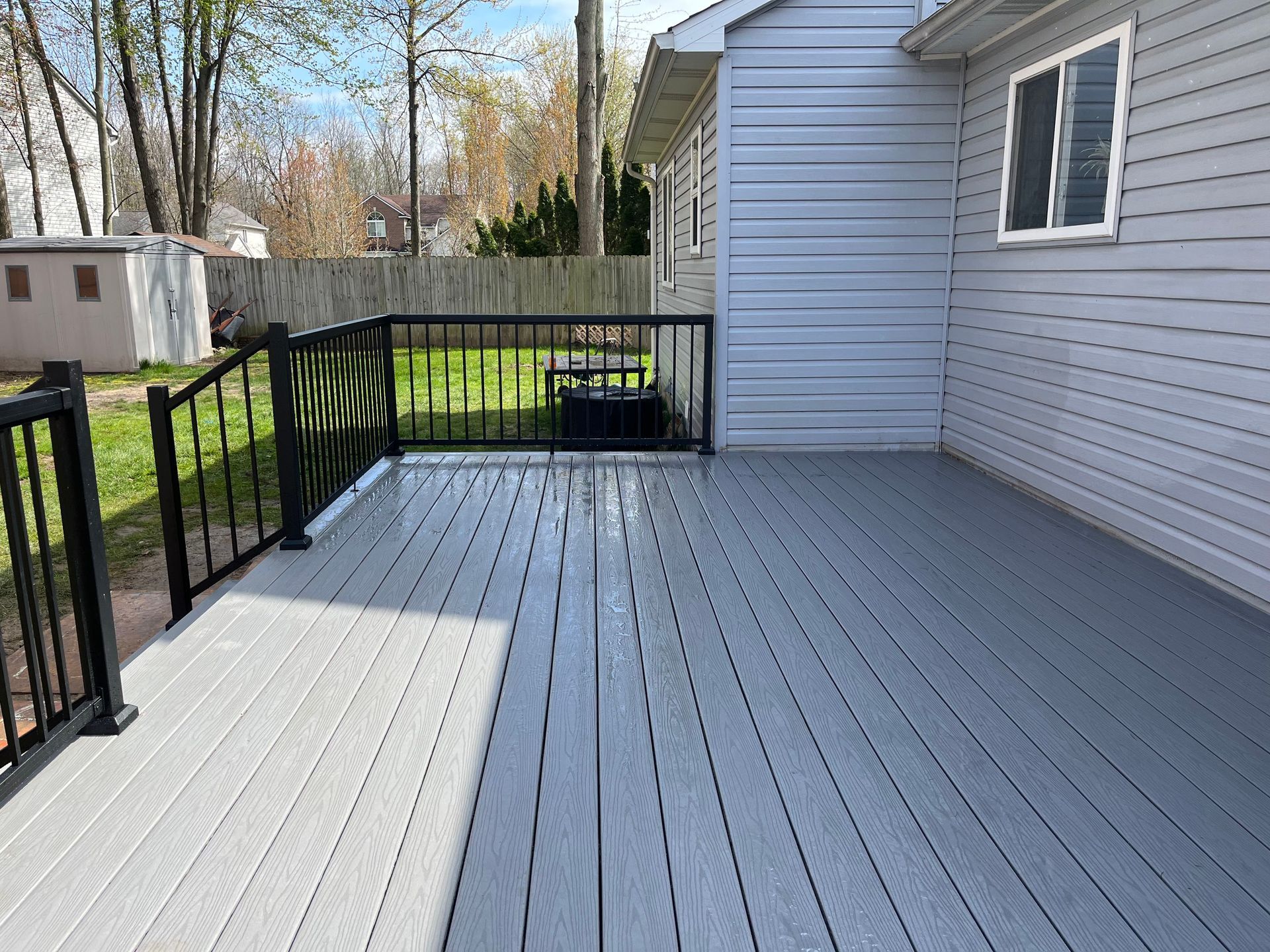 A gray deck with a black railing is in front of a white house.