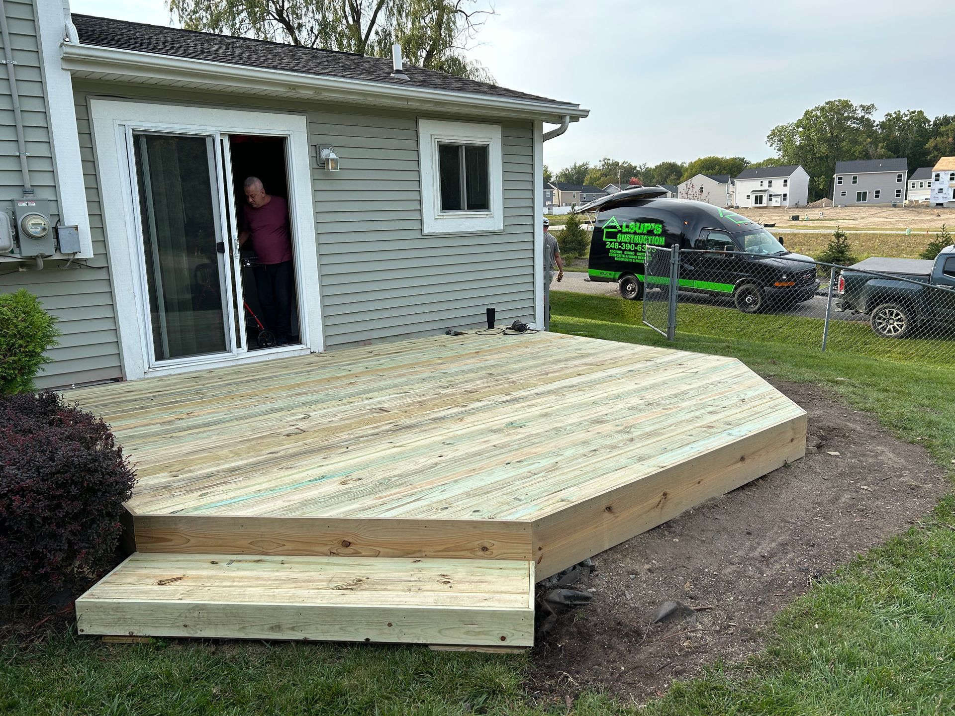 A man is standing on a wooden deck in front of a house.