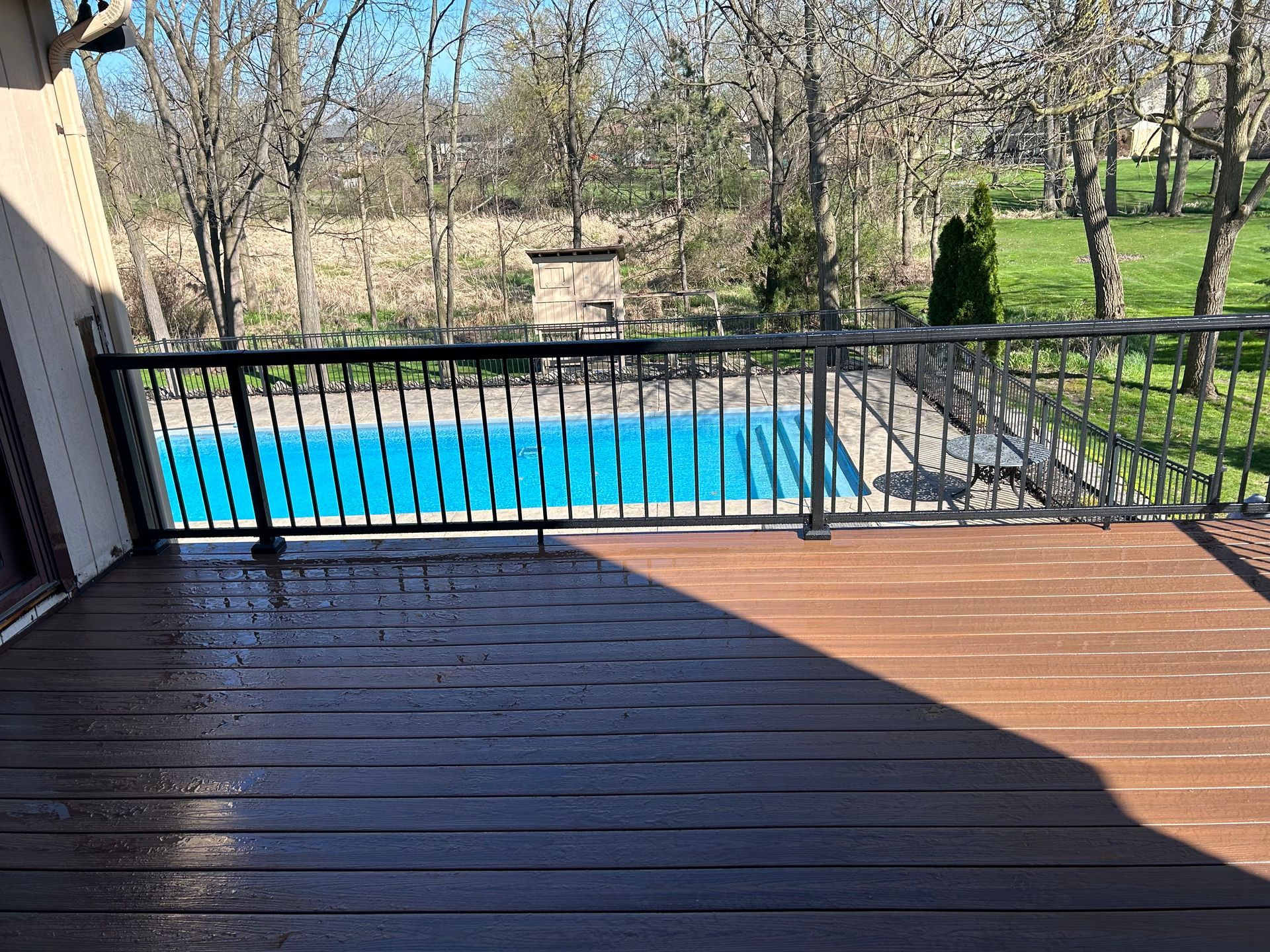 A wooden deck with a metal railing overlooking a swimming pool.
