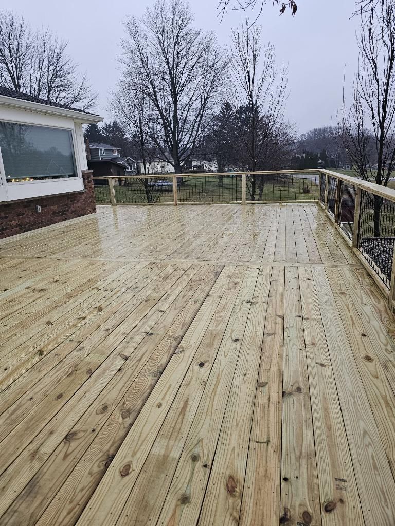 A large wooden deck with a railing and trees in the background.