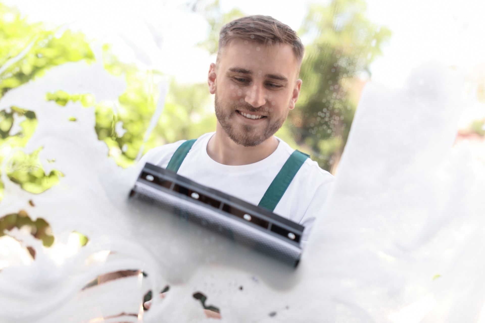 Smiling window cleaner using a squeegee to wash a glass window outdoors.