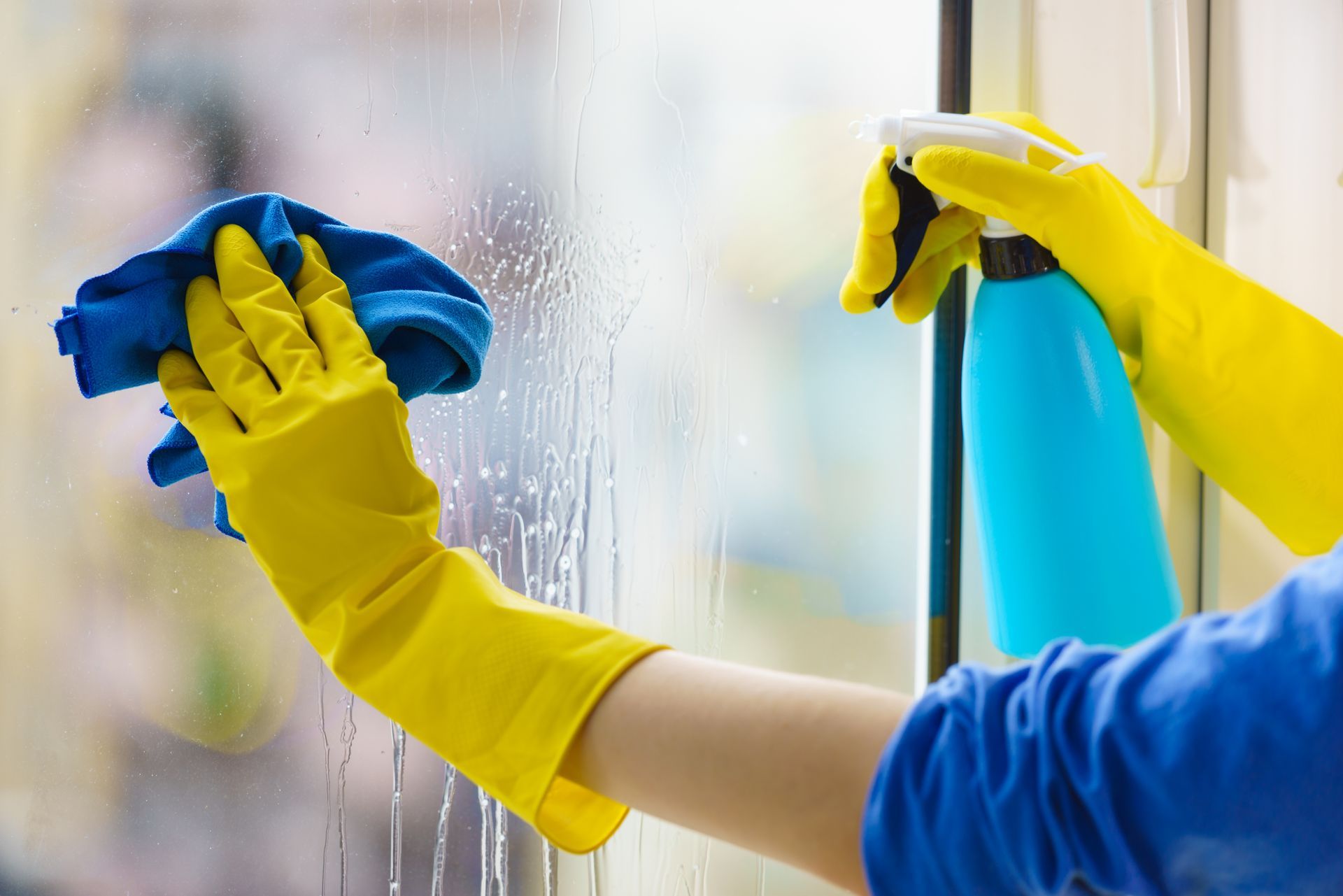A cleaning professional wiping a glass window with spray and cloth. A cleaning professional wiping a glass window with spray and cloth.