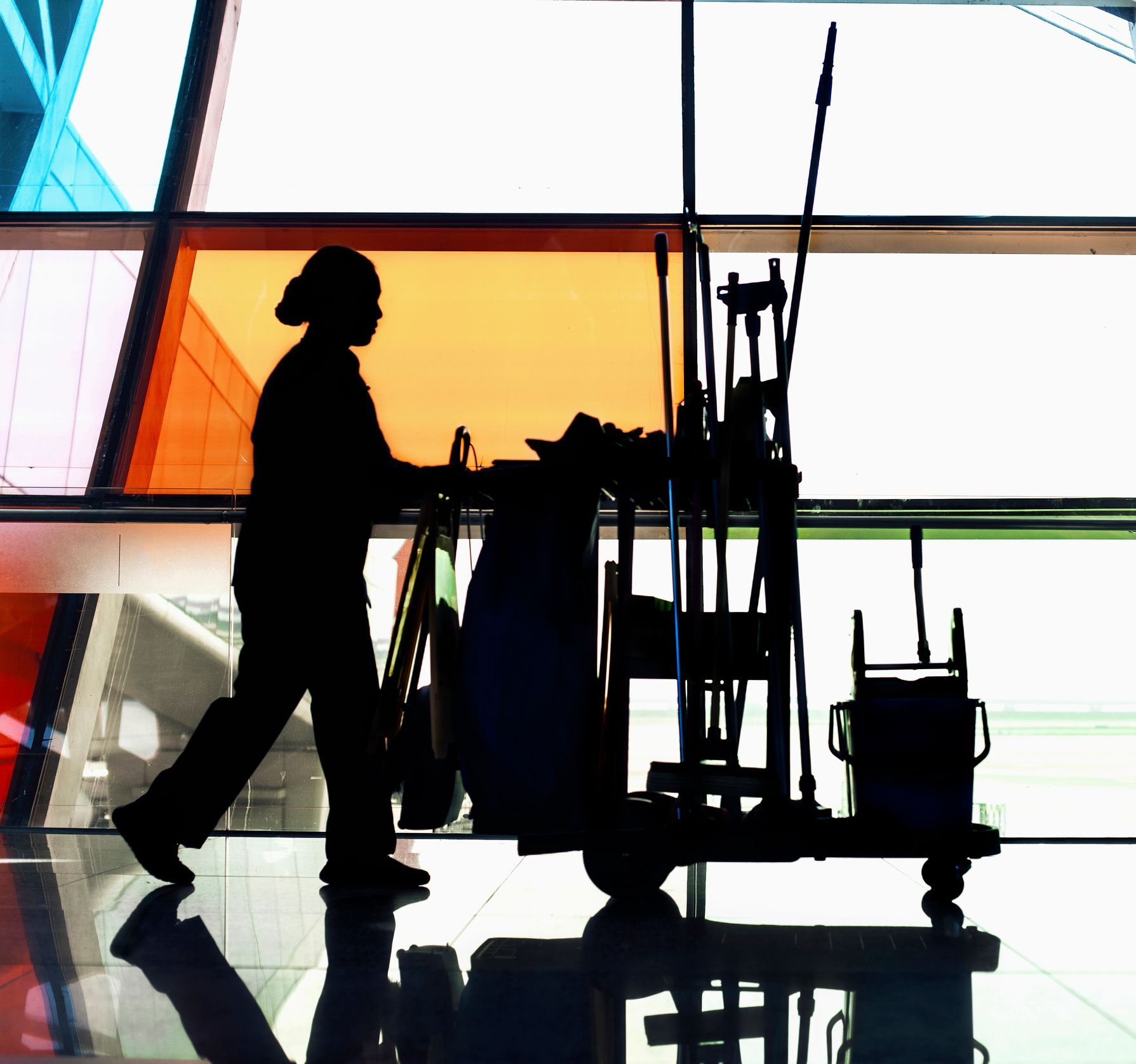Silhouette of person pushing cleaning cart by colorful glass panels.