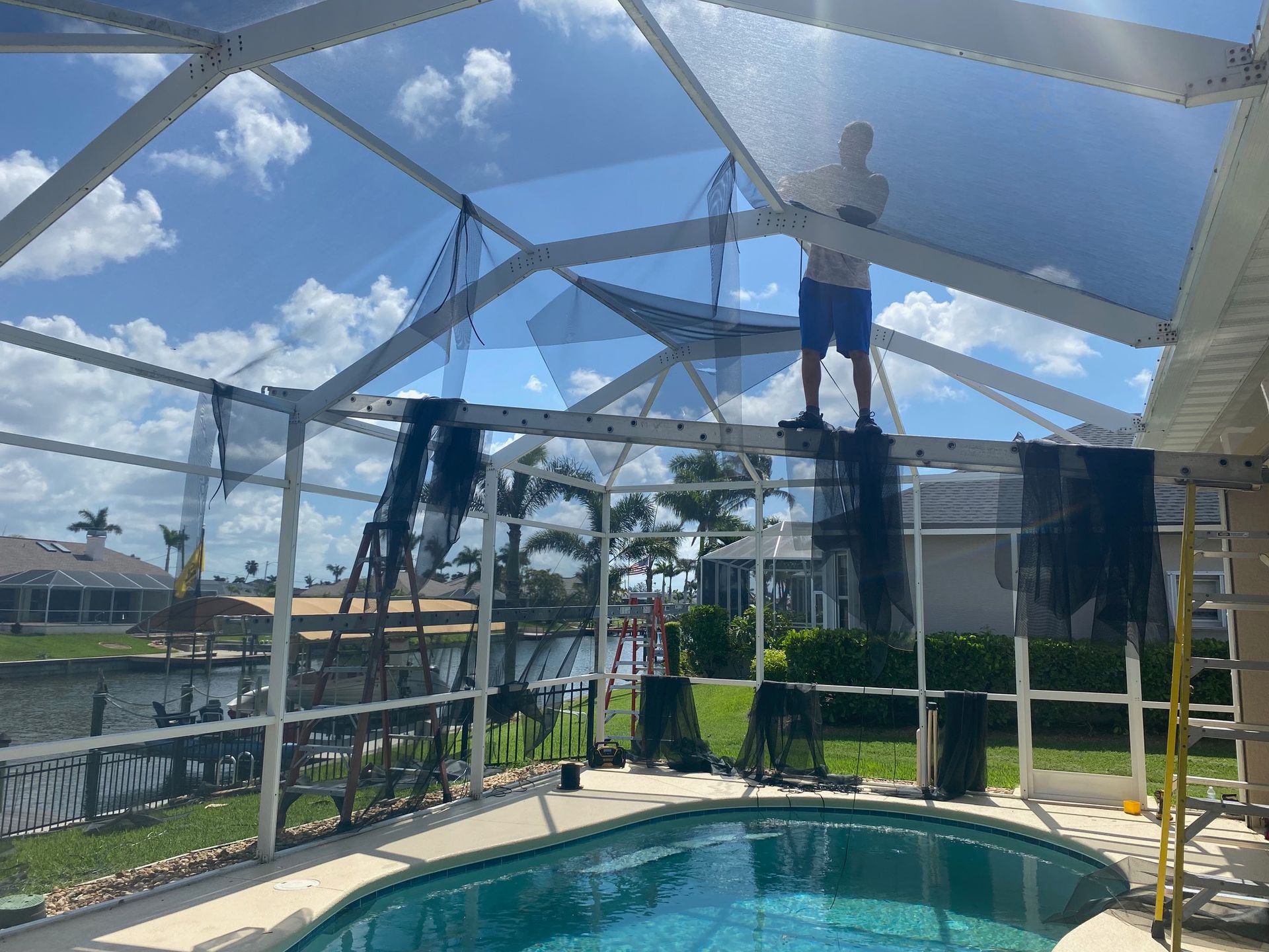 A man is standing on top of a screened in pool.