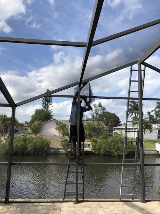 A man is standing on a ladder working on a screened in pool.