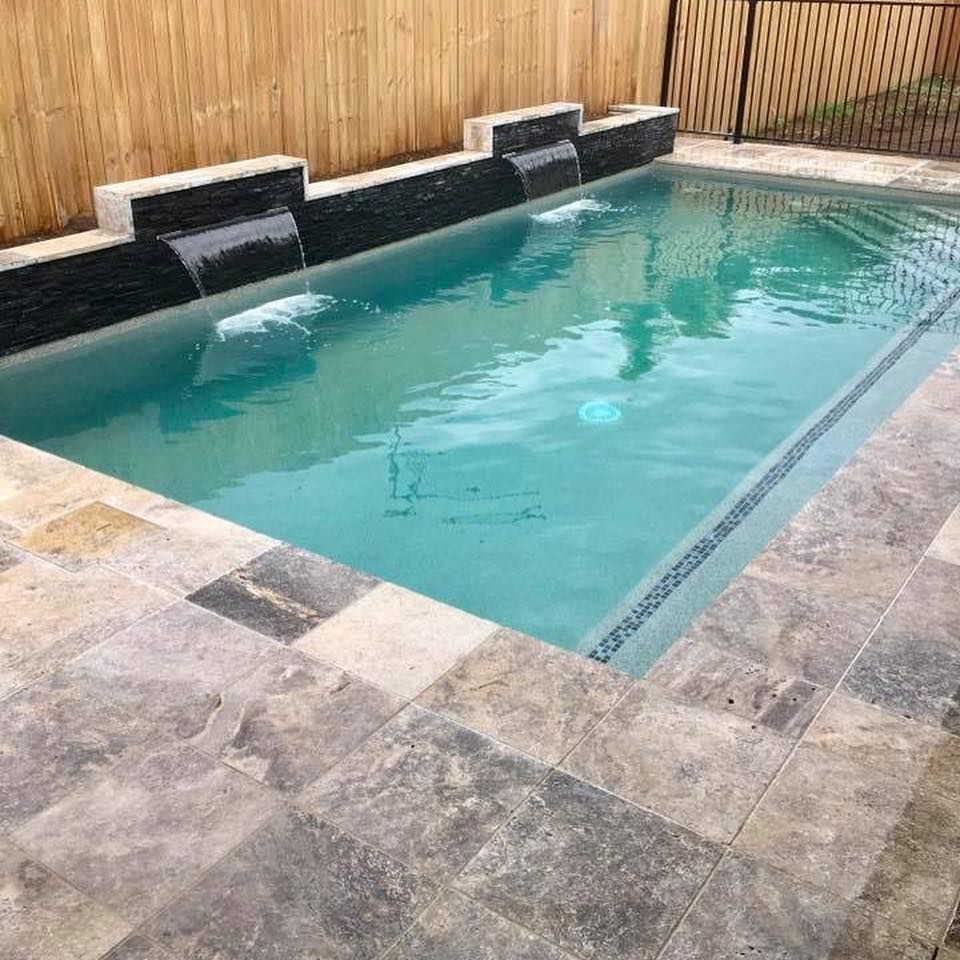 Swimming pool with waterfall feature, surrounded by stone tiles and a wooden fence— Tru Blu Pools & Spas in Bluewater, QLD