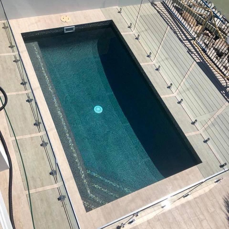 Rectangular swimming pool surrounded by beige decking, glass railing, and dark blue water— Tru Blu Pools & Spas in Bluewater, QLD