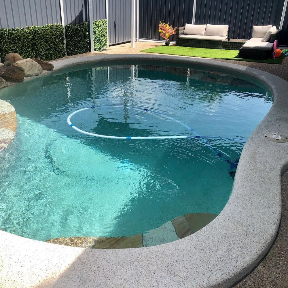Swimming pool with clear blue water and concrete edging. Lush greenery and outdoor seating in the background— Tru Blu Pools & Spas in Bluewater, QLD