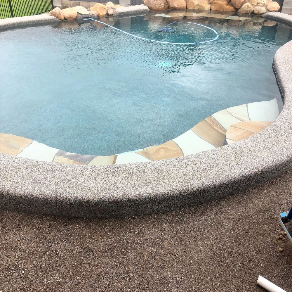 Pool with a gray pebble finish, clear blue water, and stone accents— Tru Blu Pools & Spas in Bluewater, QLD