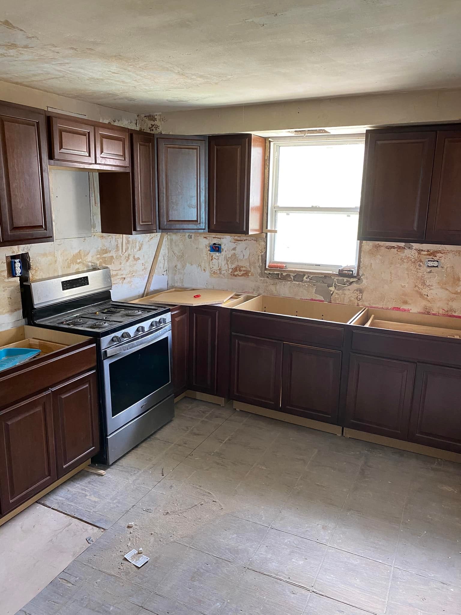 A kitchen with a stove , sink , cabinets and a window.