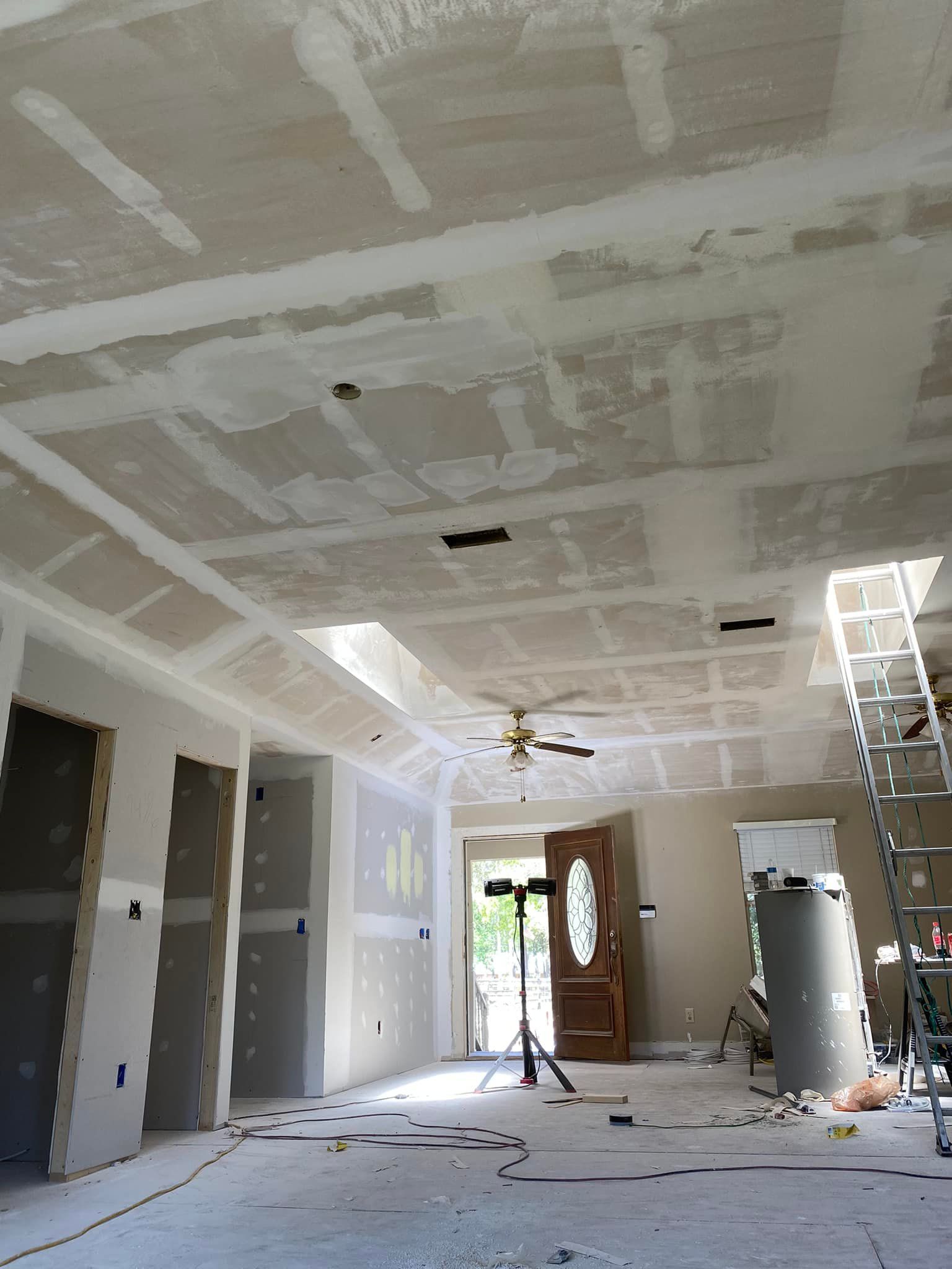A living room under construction with a ceiling fan and a ladder.