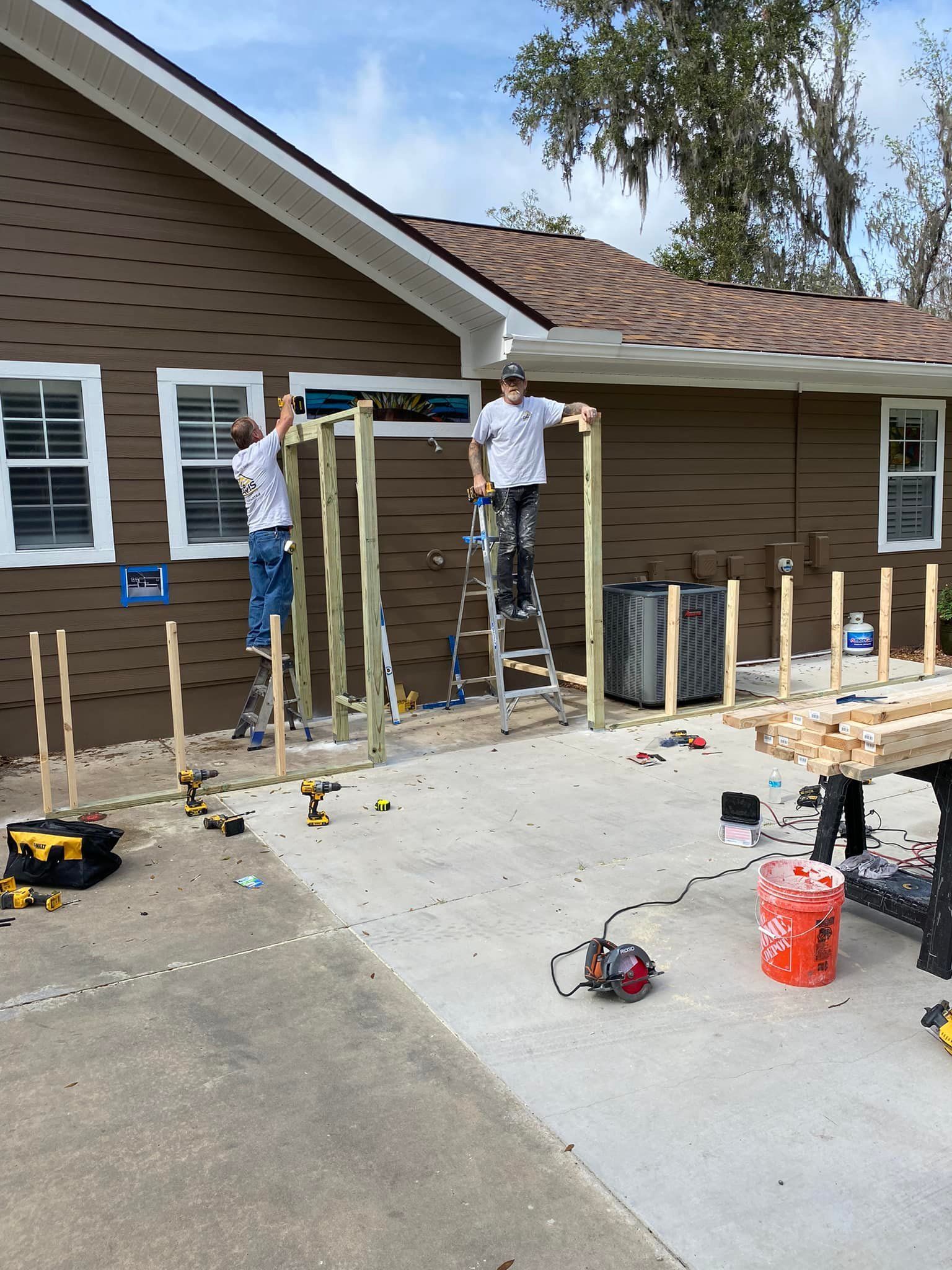 Two men are working on a wooden structure in front of a house.