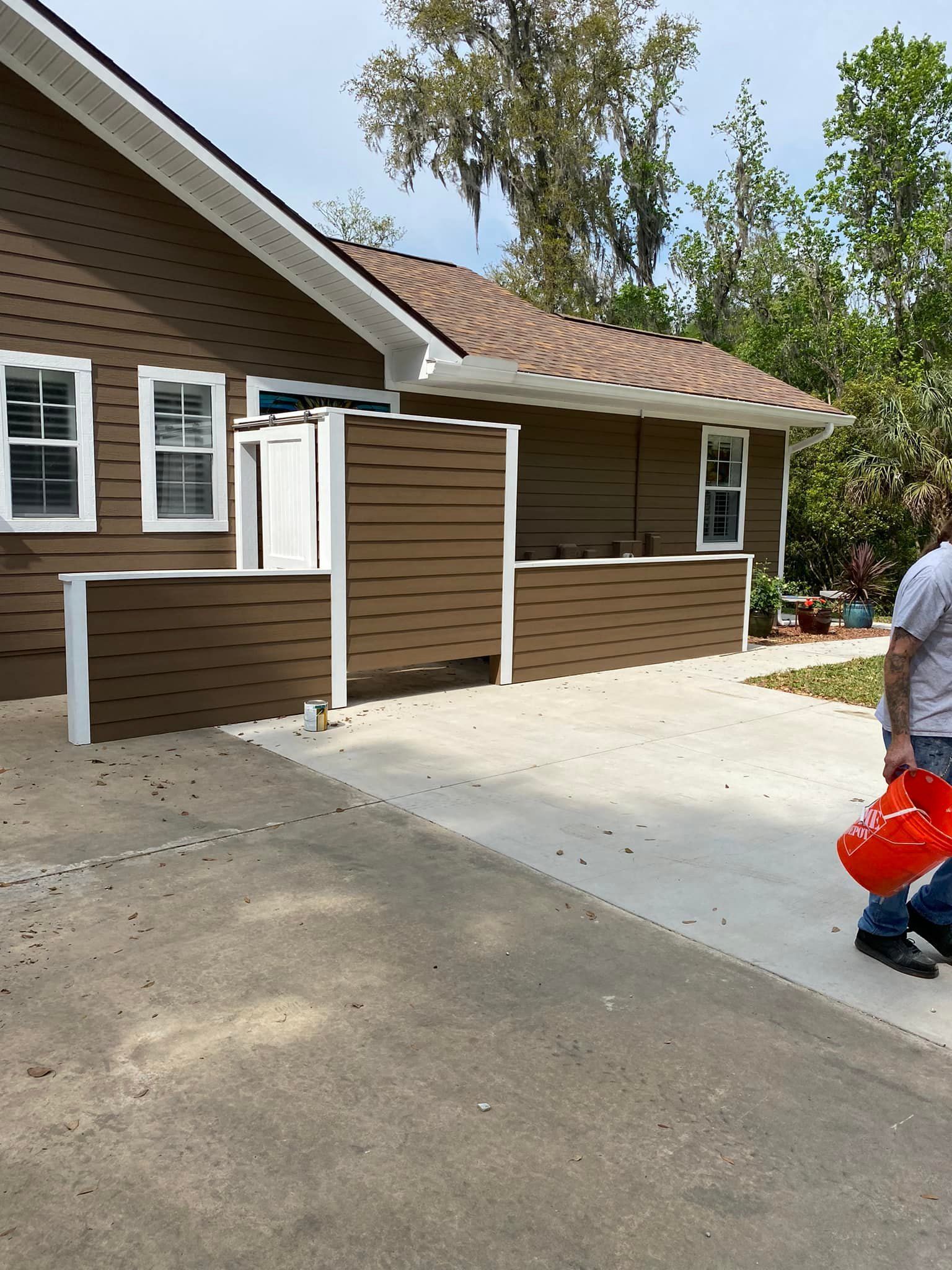 A man is walking down a sidewalk in front of a brown house