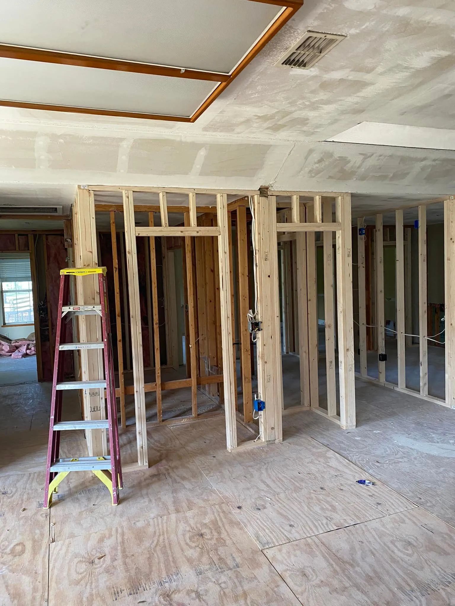 Interior renovation: unfinished wooden wall frames, ladder, plywood floor.