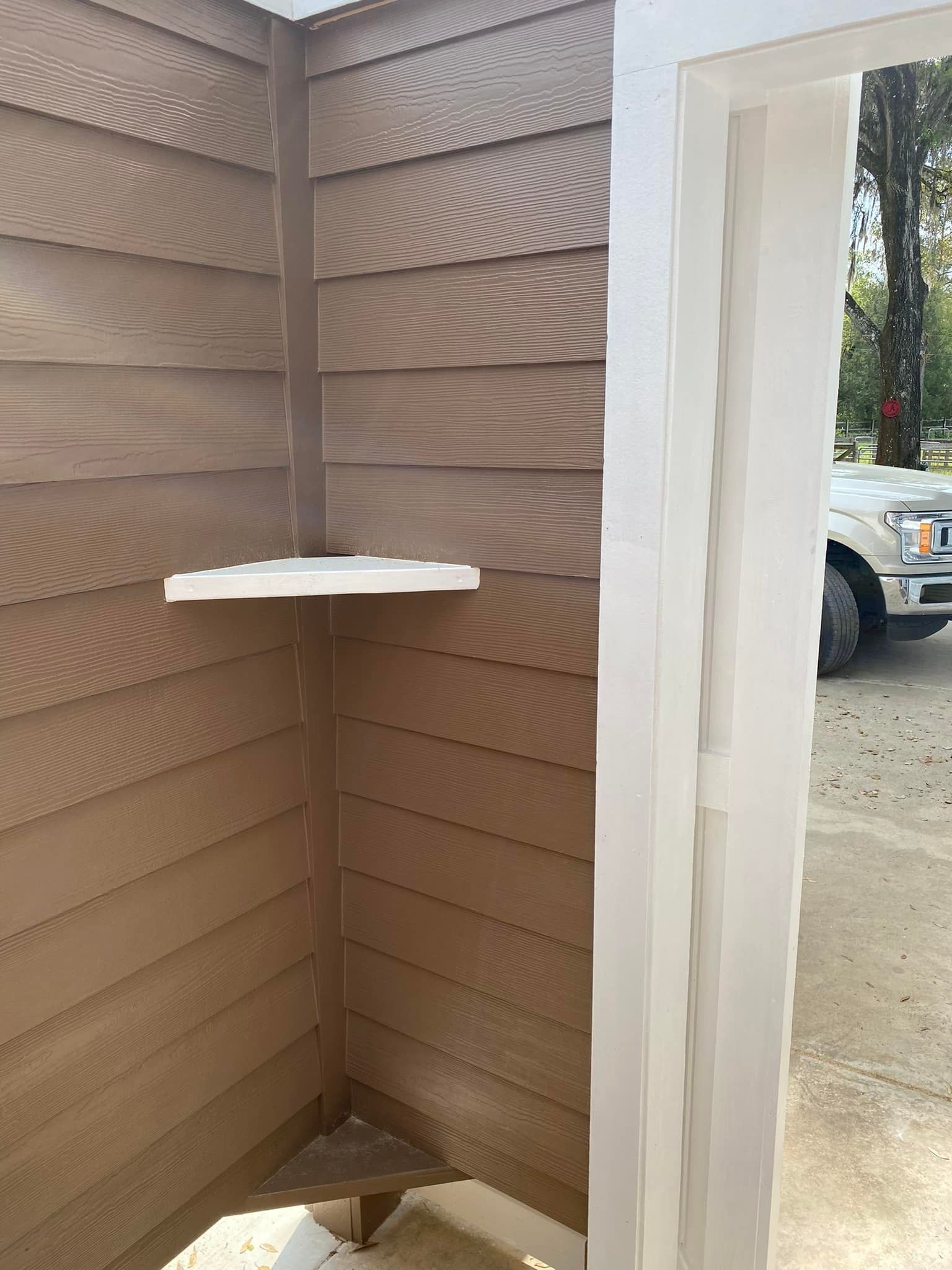A brown house with a white shelf on the side of it.