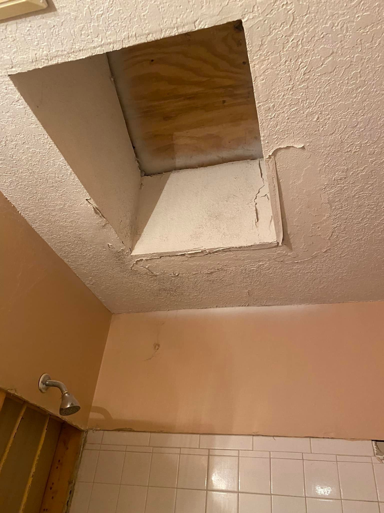 A bathroom with a hole in the ceiling and a shower head.