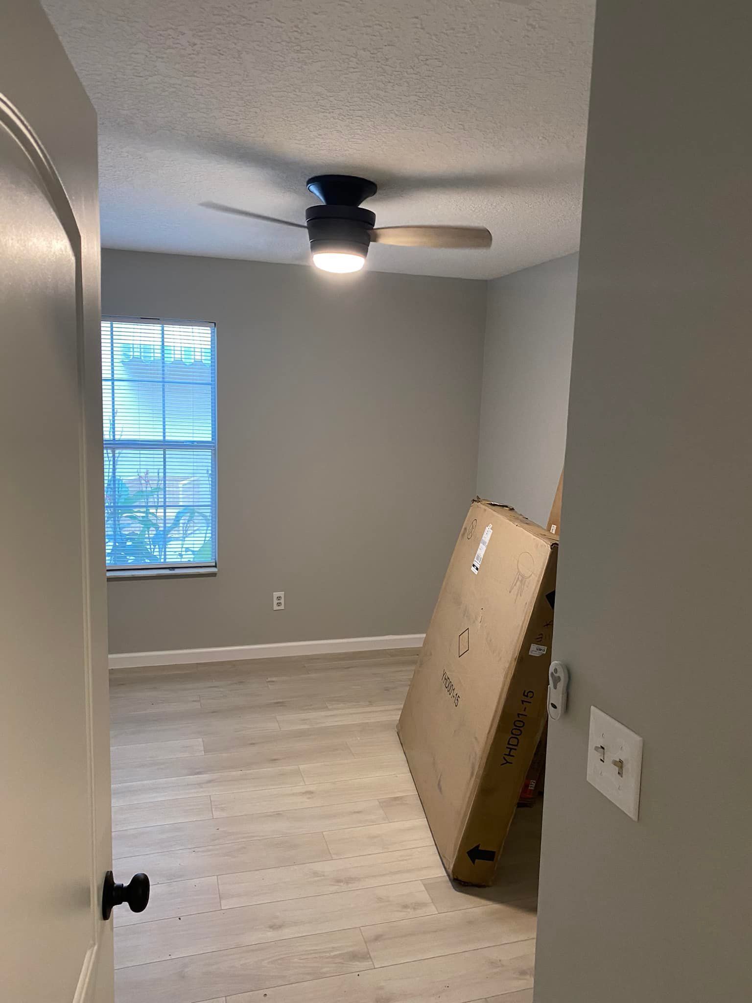 A bedroom with a ceiling fan and a box on the floor.