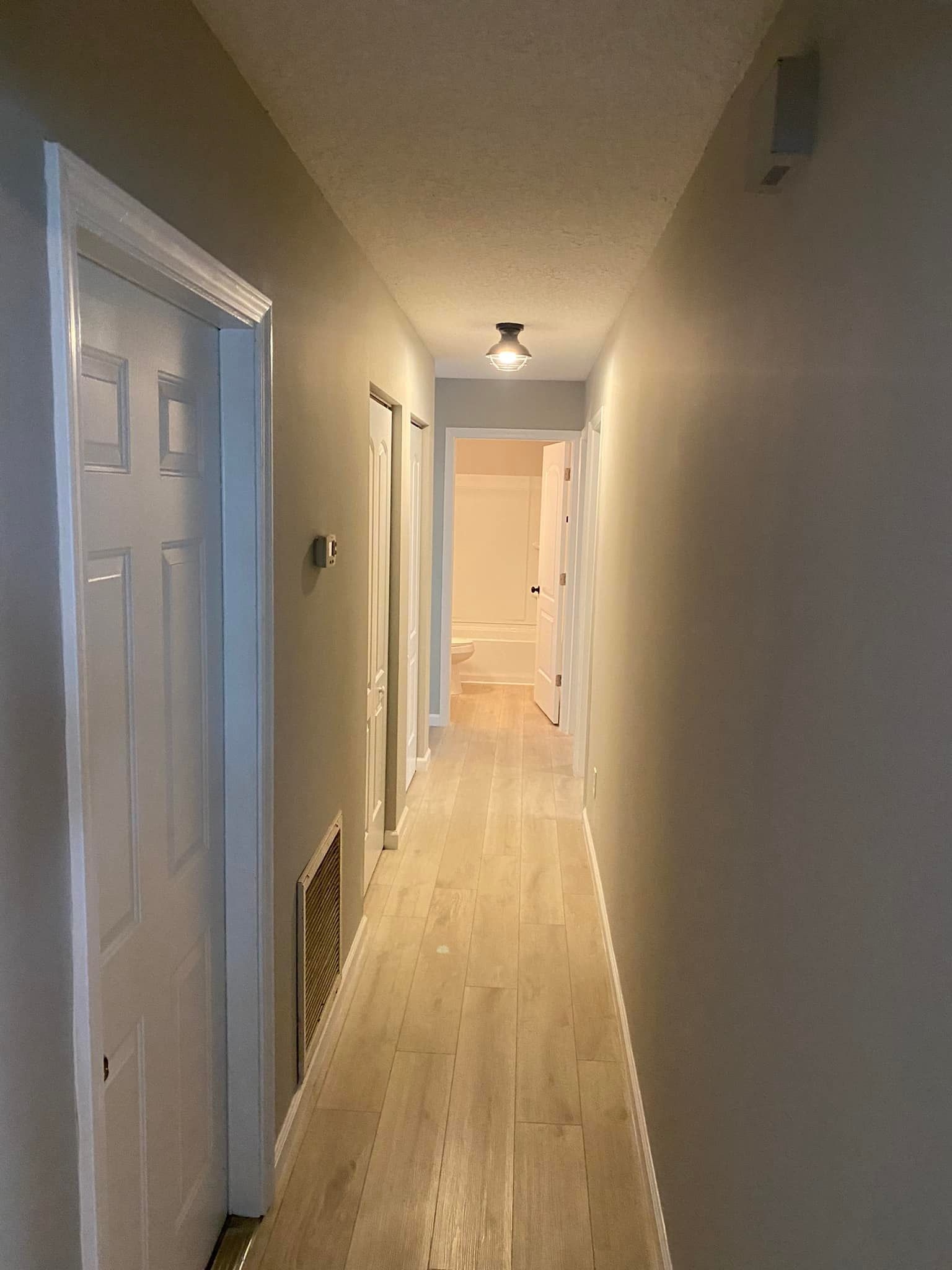 A long hallway with hardwood floors and gray walls leading to a bathroom.