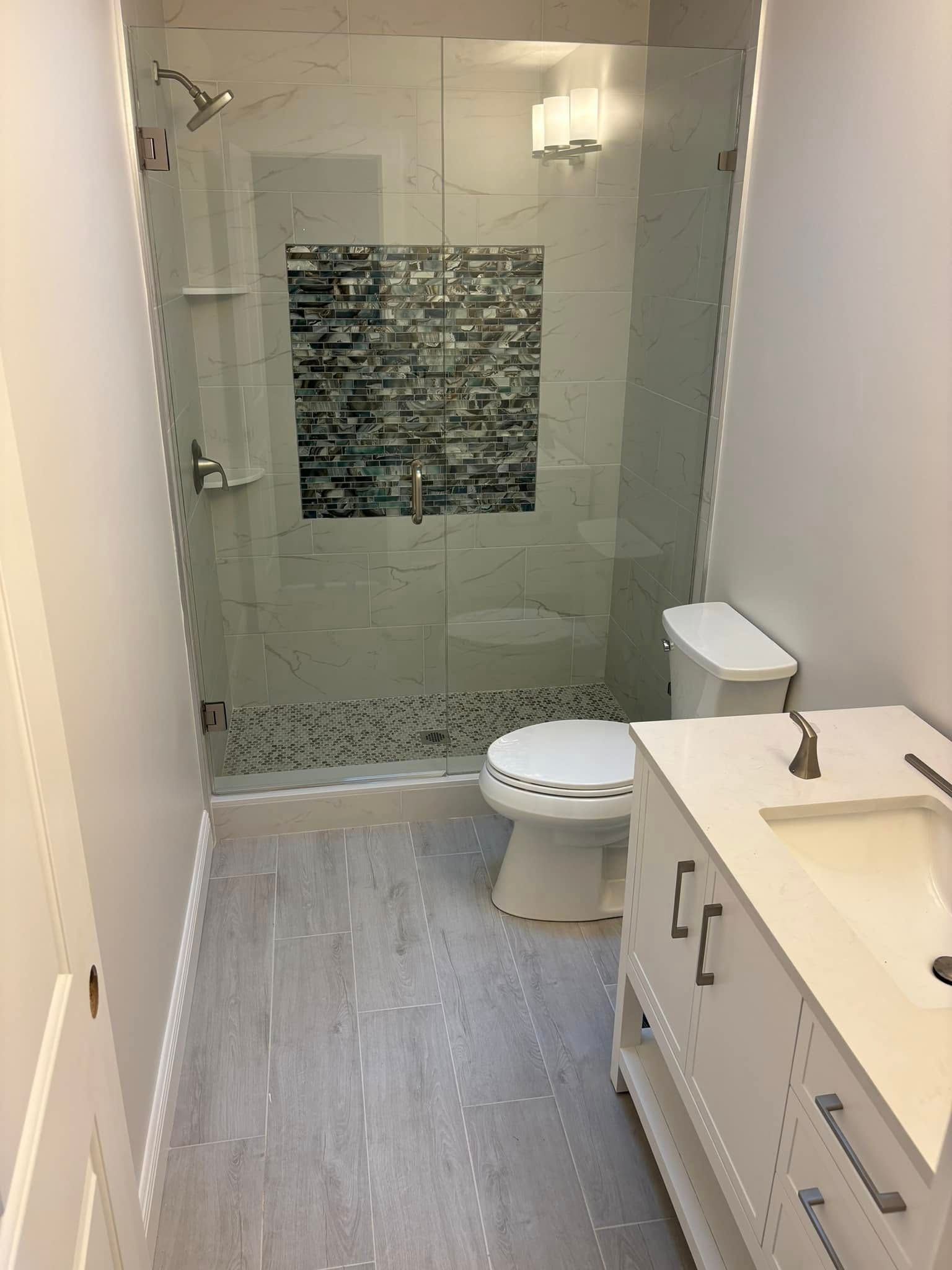 Small modern bathroom with glass shower, toilet, and white vanity with sink.