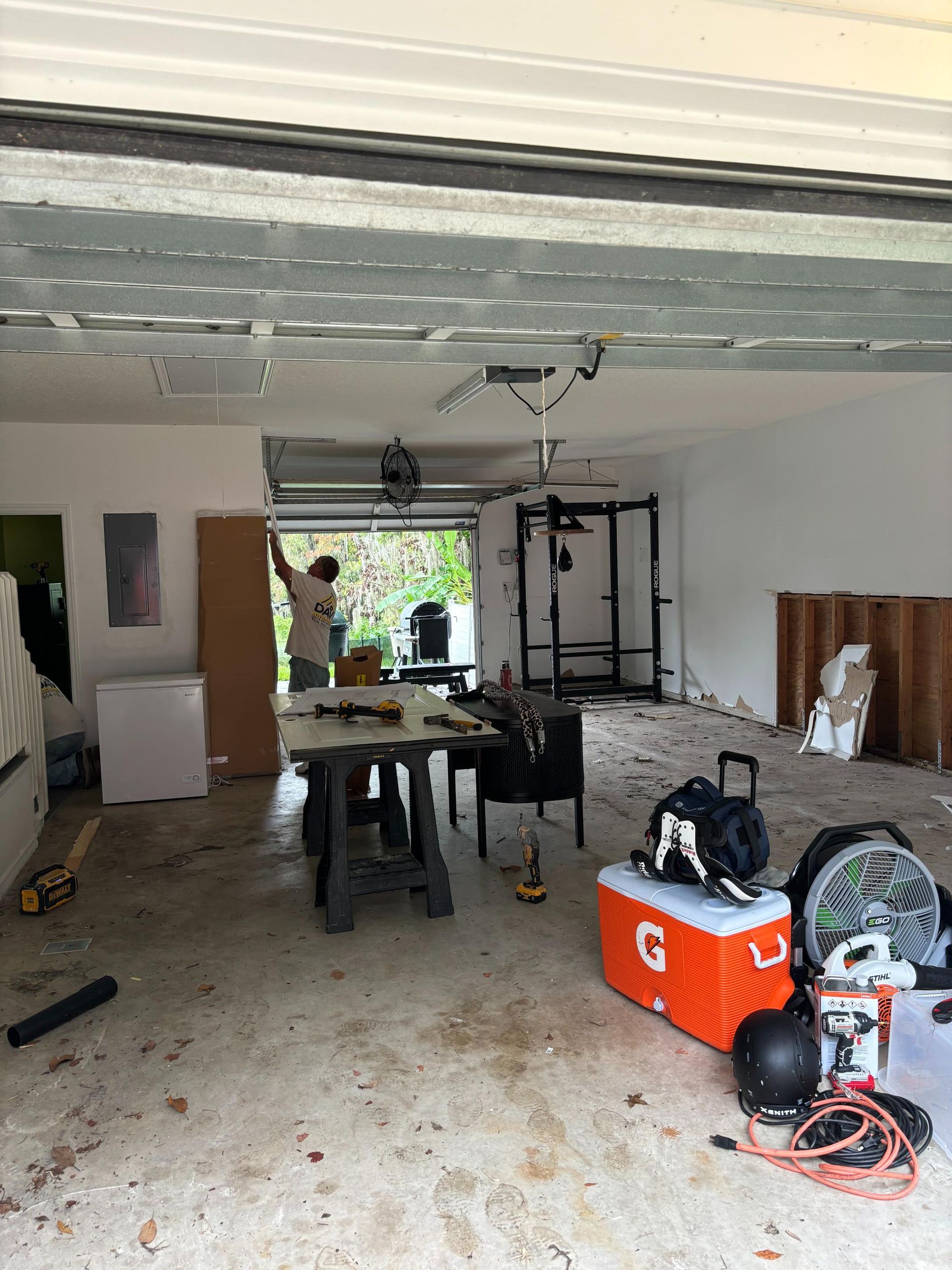 Garage interior with construction in progress; person working at a table, weight rack visible.