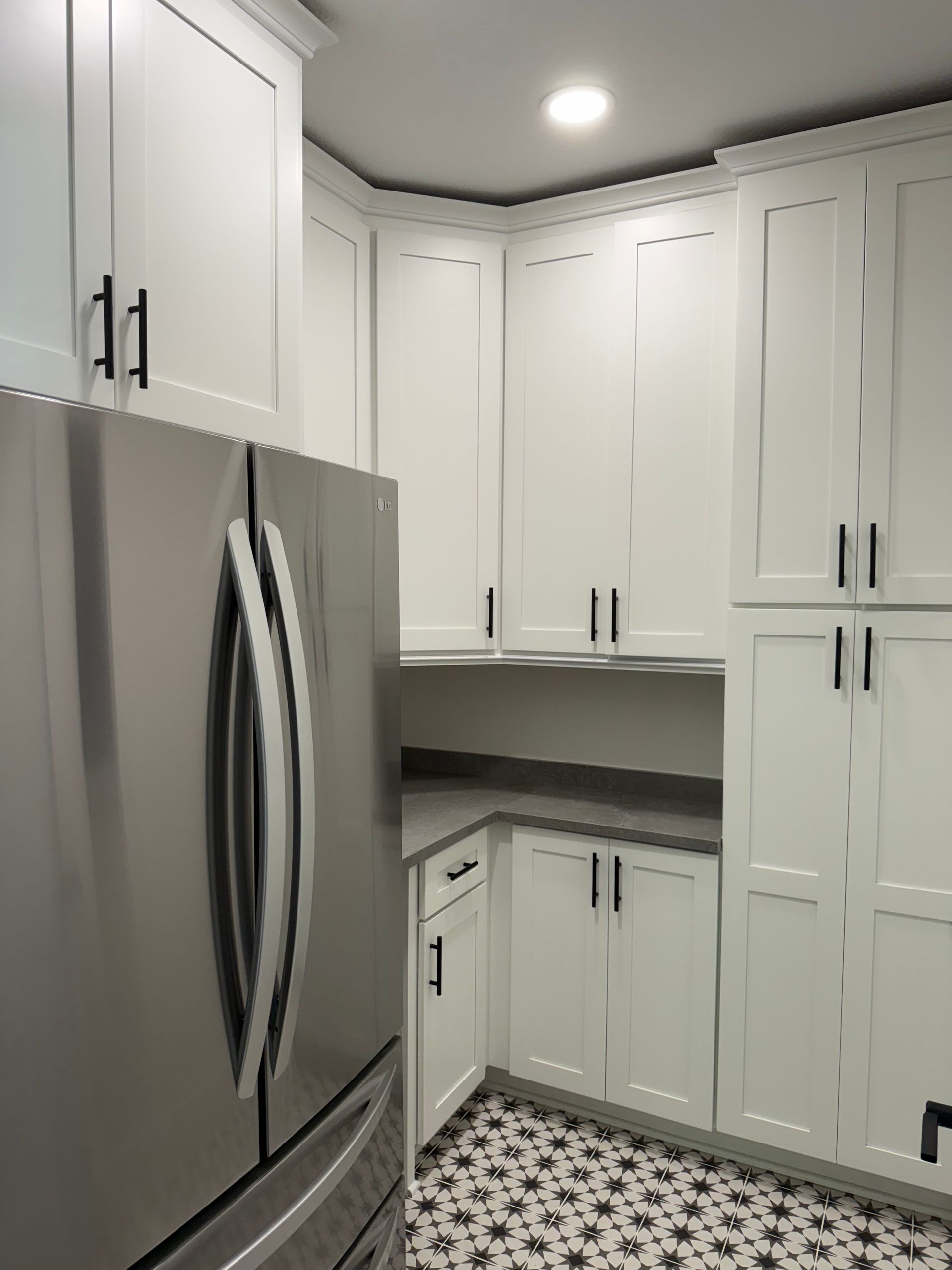 White kitchen cabinets with black hardware next to a stainless steel refrigerator. Patterned tile floor.