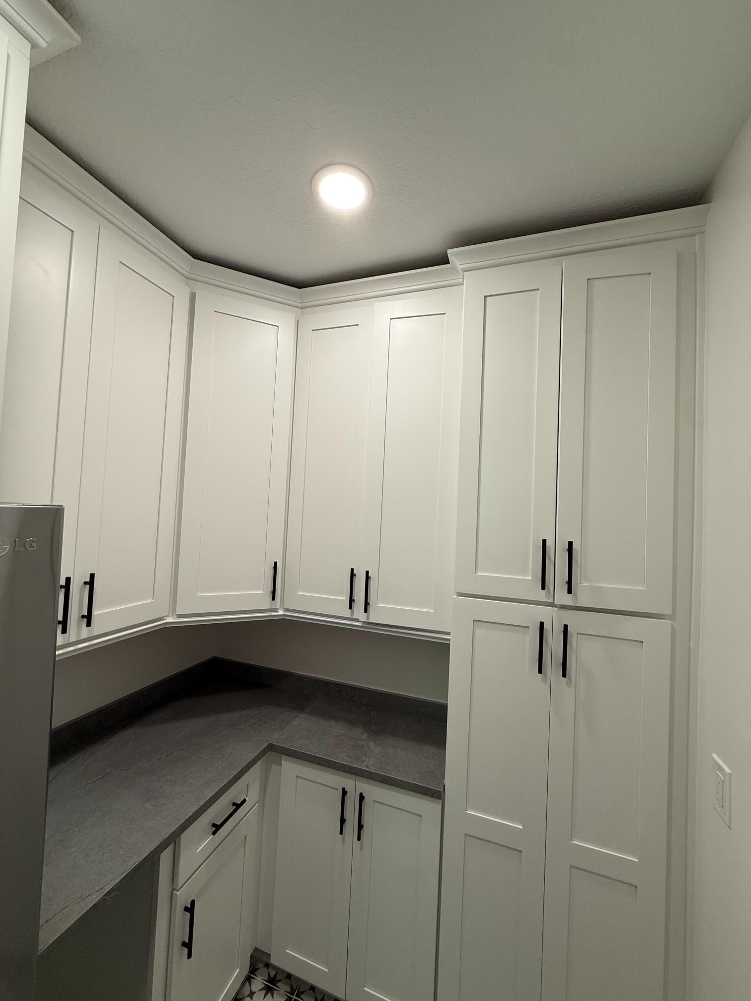 White kitchen cabinets with black hardware and gray countertop in a small corner space.