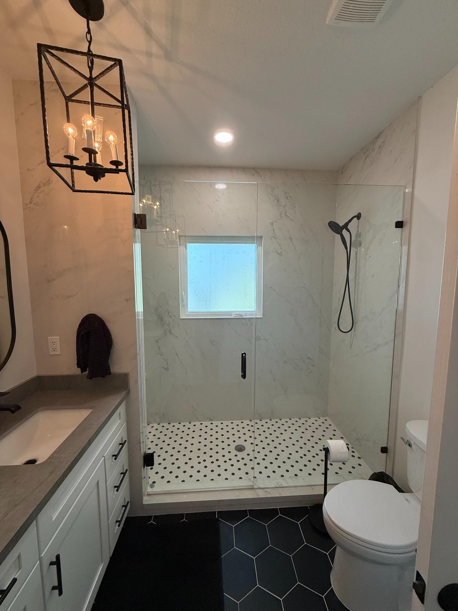 Modern bathroom with marble shower, black fixtures, hexagon and penny tile floors.