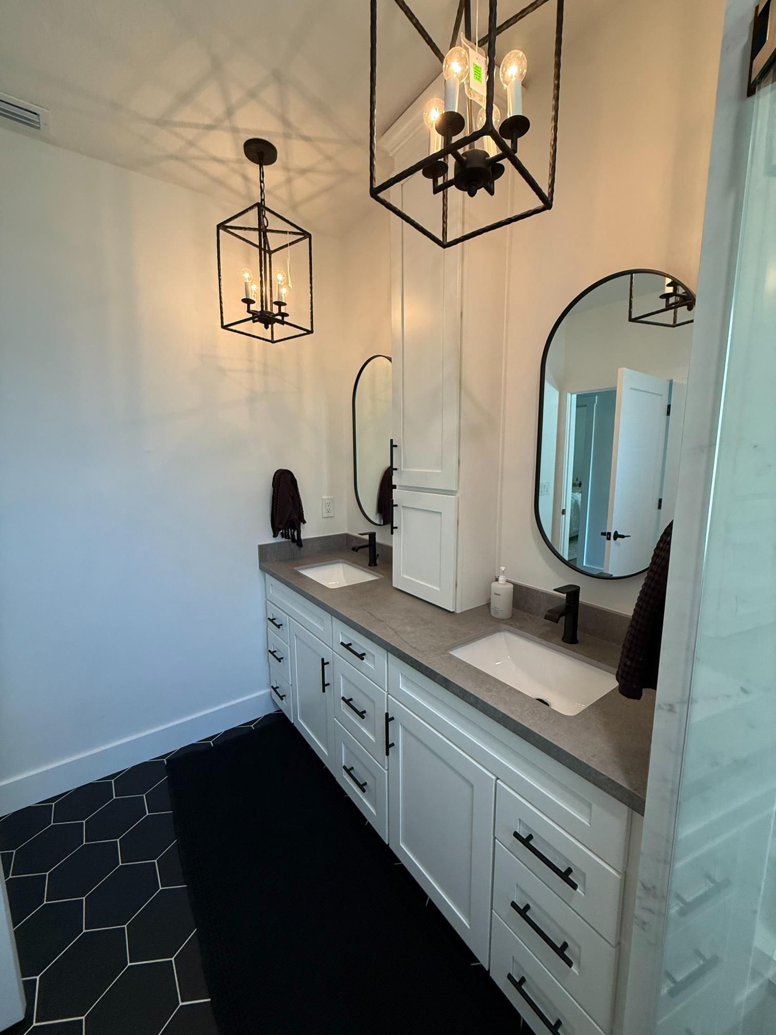 Bathroom with white cabinetry, gray countertop, black hardware, black mirrors, and hexagon tile flooring.