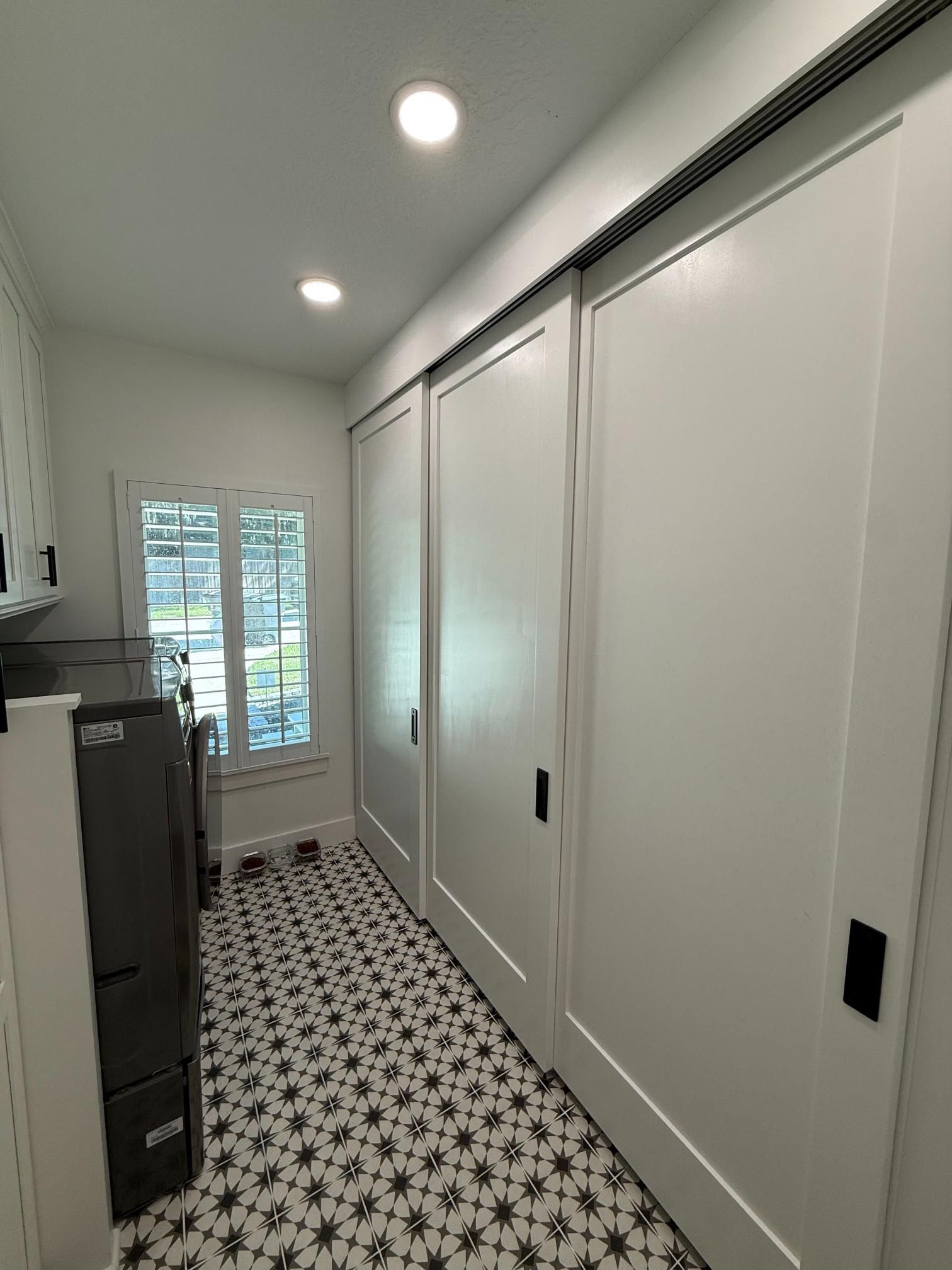 Laundry room with white sliding doors, patterned floor, window.