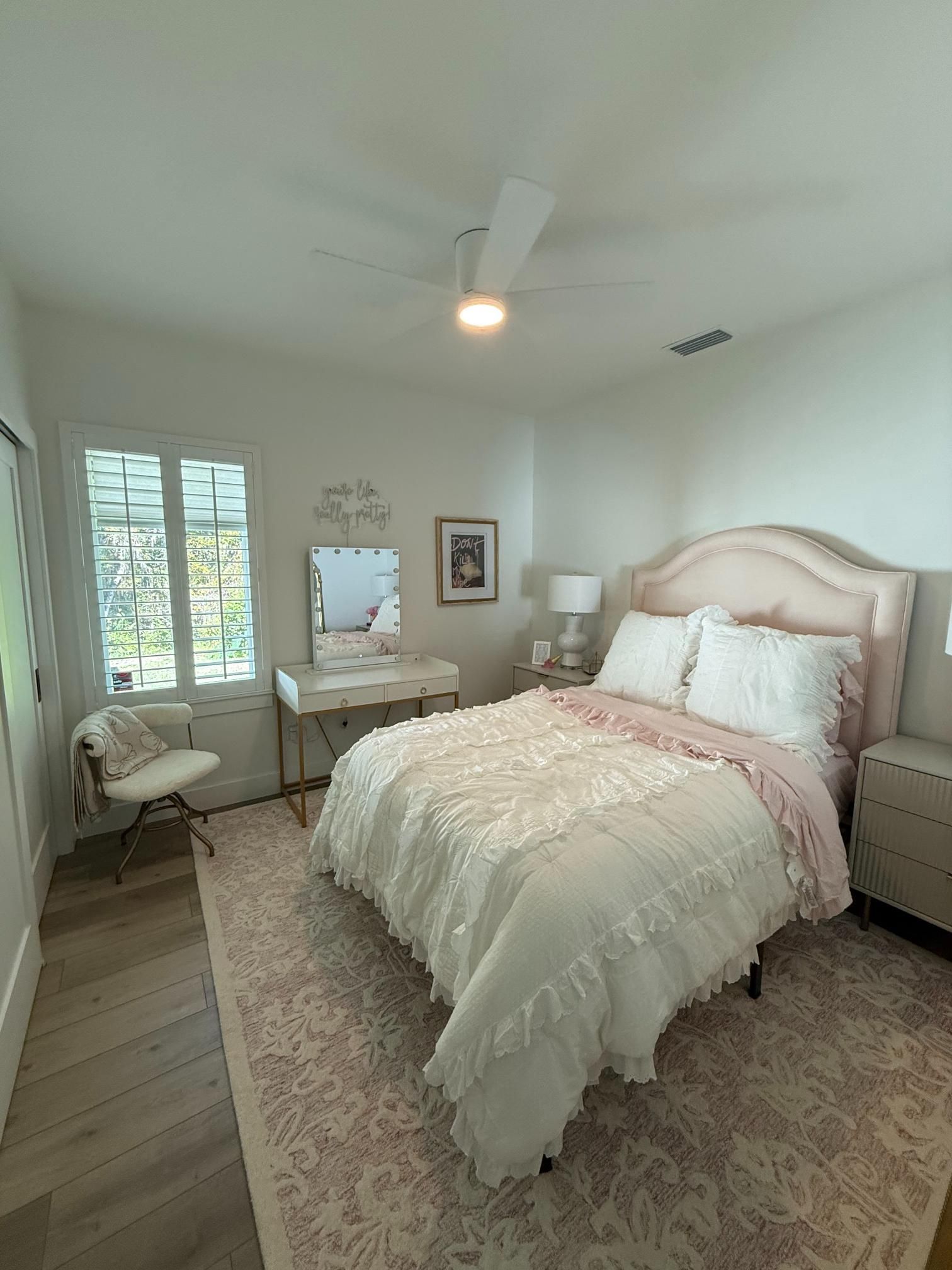 Bedroom with pink and white decor; bed, vanity, chair, rug.