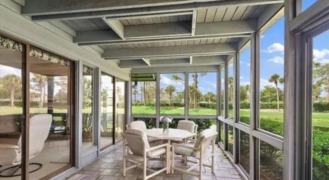 A screened in porch with a table and chairs and a view of a golf course.