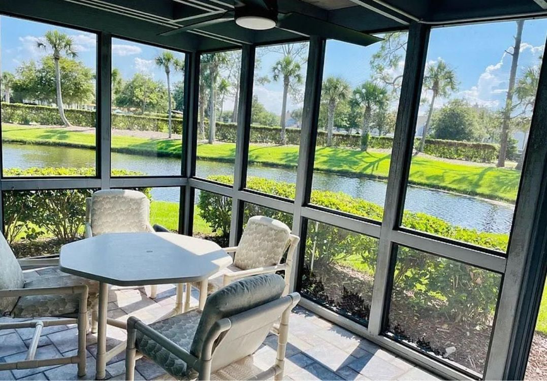 A screened in porch with a table and chairs and a view of a lake.