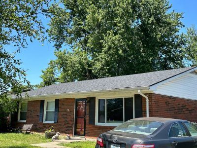 A black car is parked in front of a brick house.