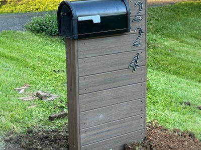 A black mailbox is sitting on top of a wooden post in the grass.