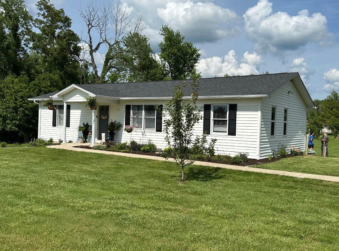 A white house with a black roof is sitting on top of a lush green field.