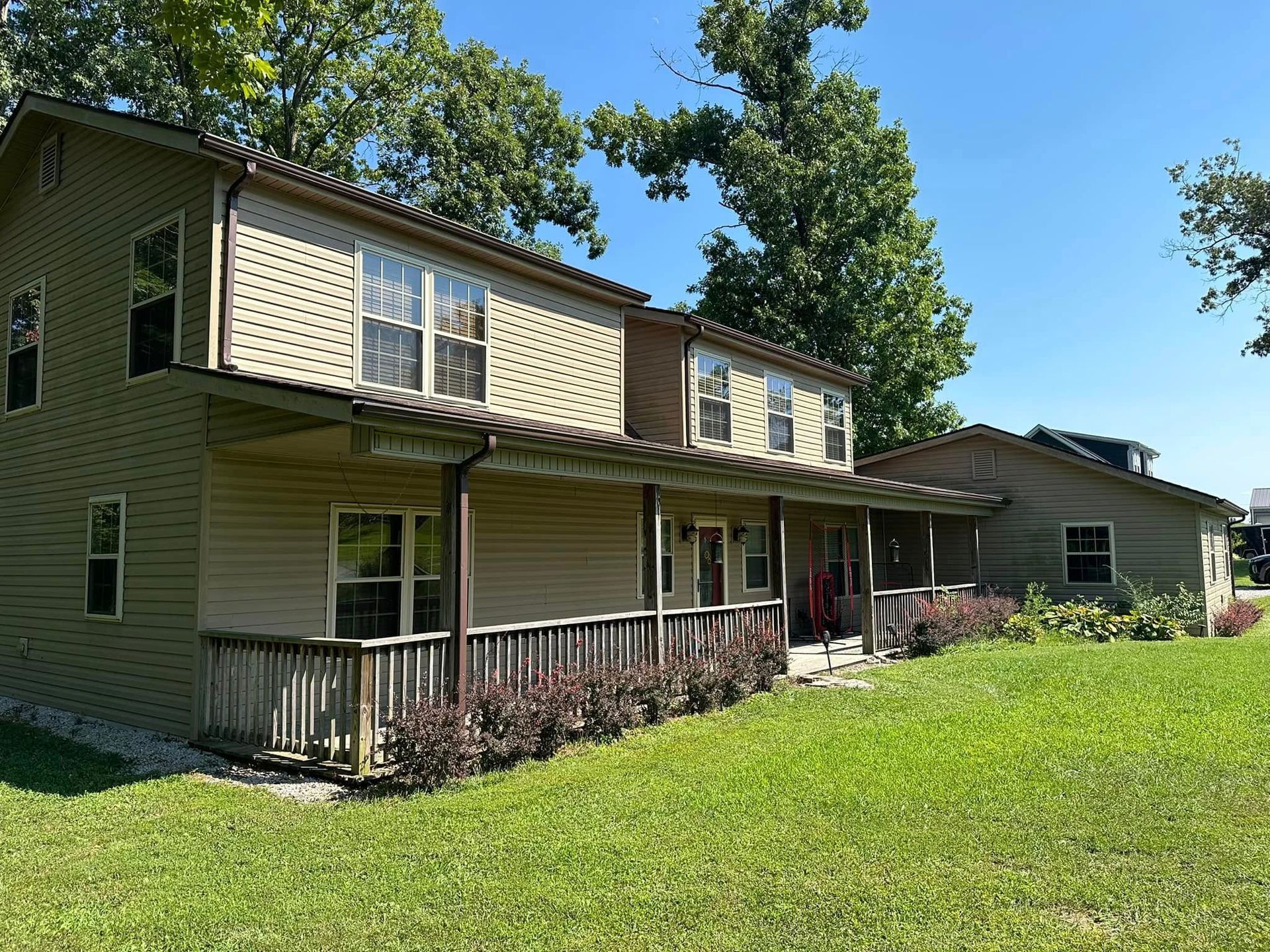 A large house with a porch and a lot of windows is sitting on top of a lush green field.